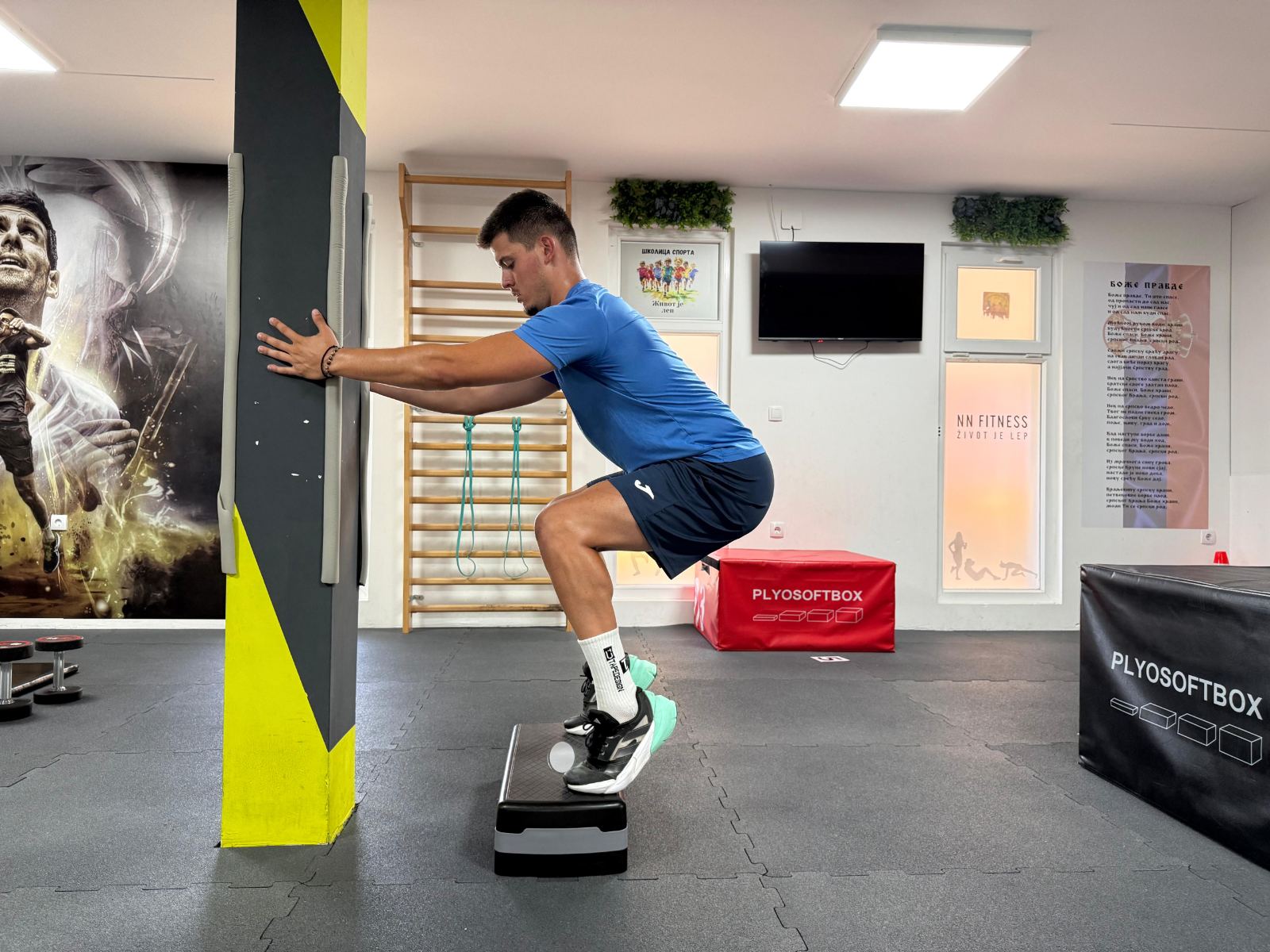 Sportista radi step-up na step platformi uz oslonac na zid