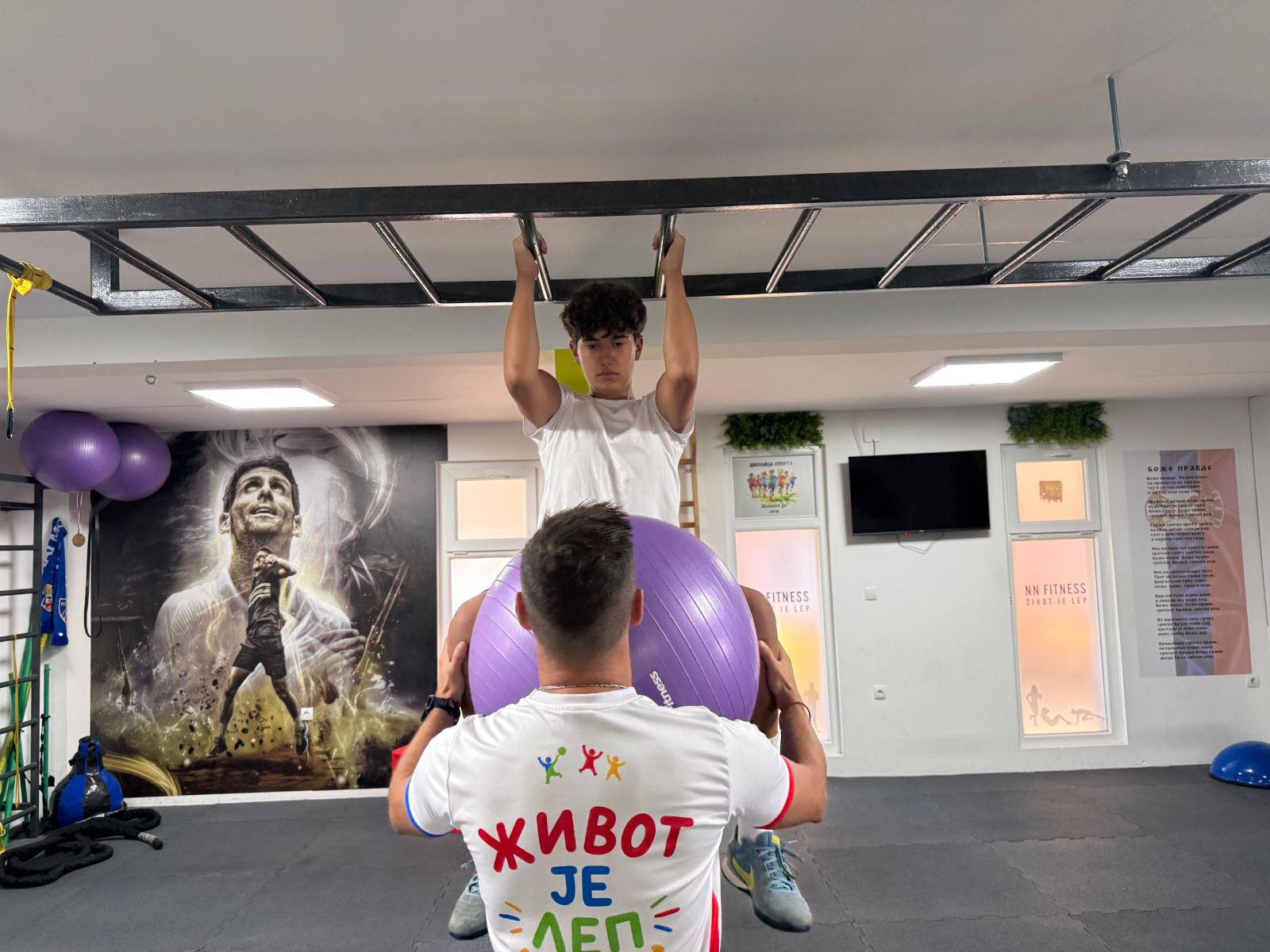 Trener asistira mladom sportisti tokom vežbe na letvenici sa fit loptom
