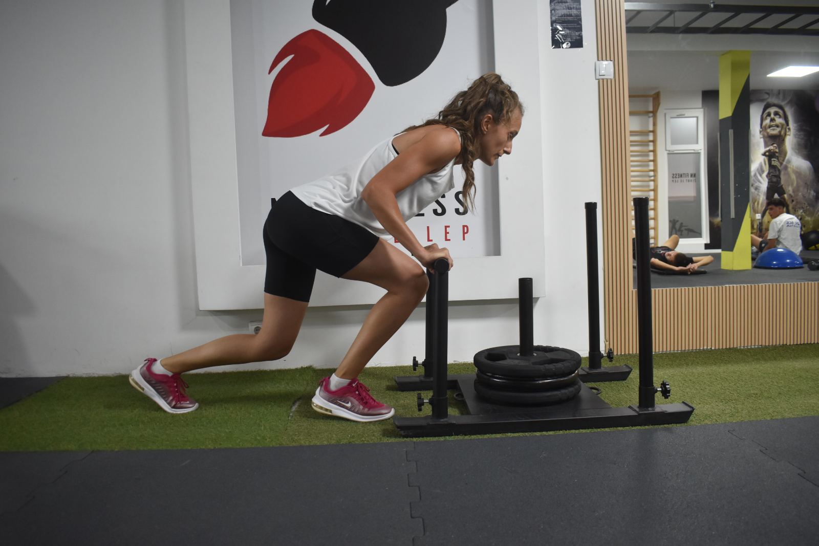 Vežbačica potiskuje sled sa tegovima u NN Fitnessu